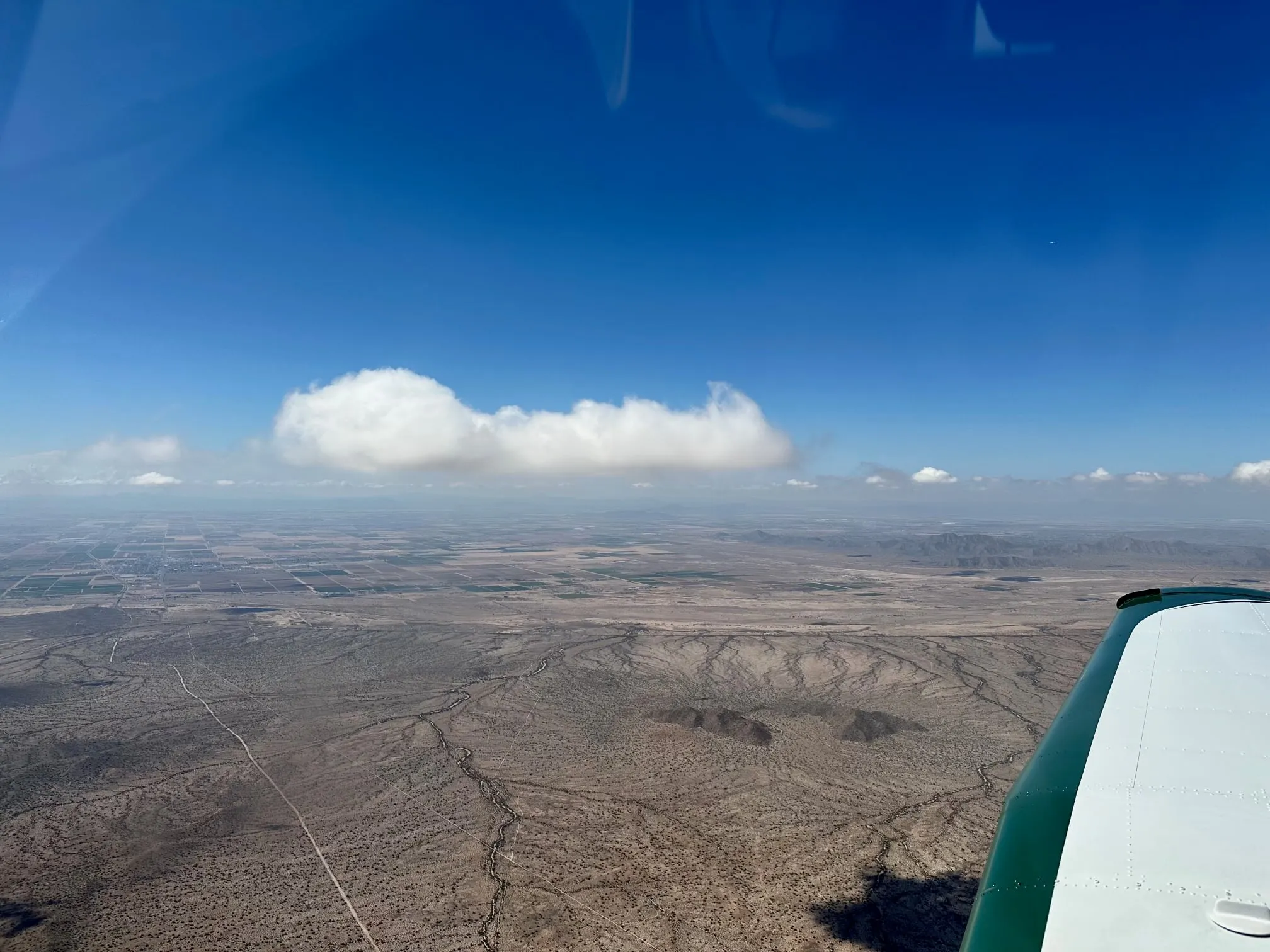 A cloud over desert ridges, the wingtip at the edge of the frame