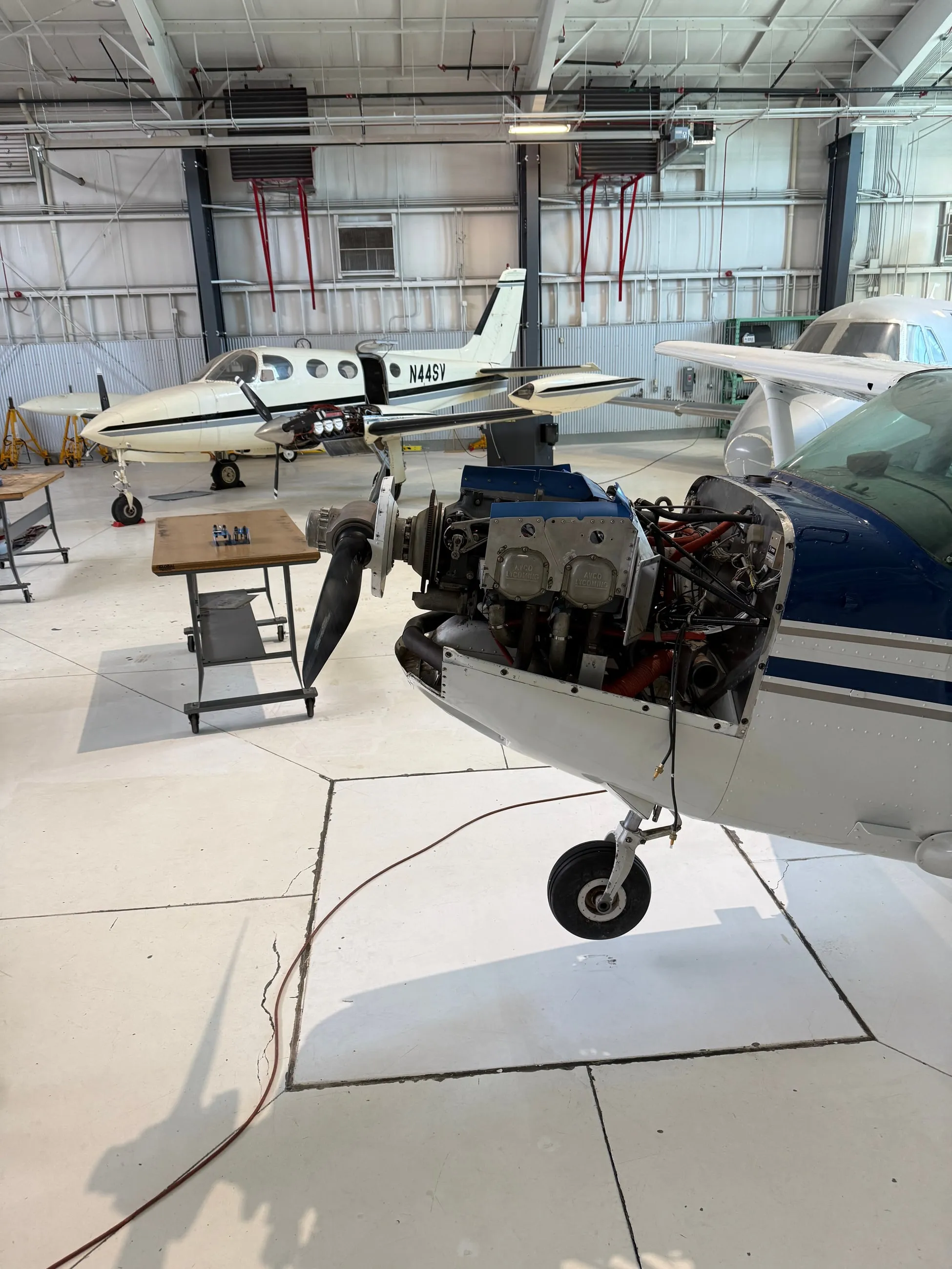 In the hangar, an airplane with its cowling off and the engine open for maintenance