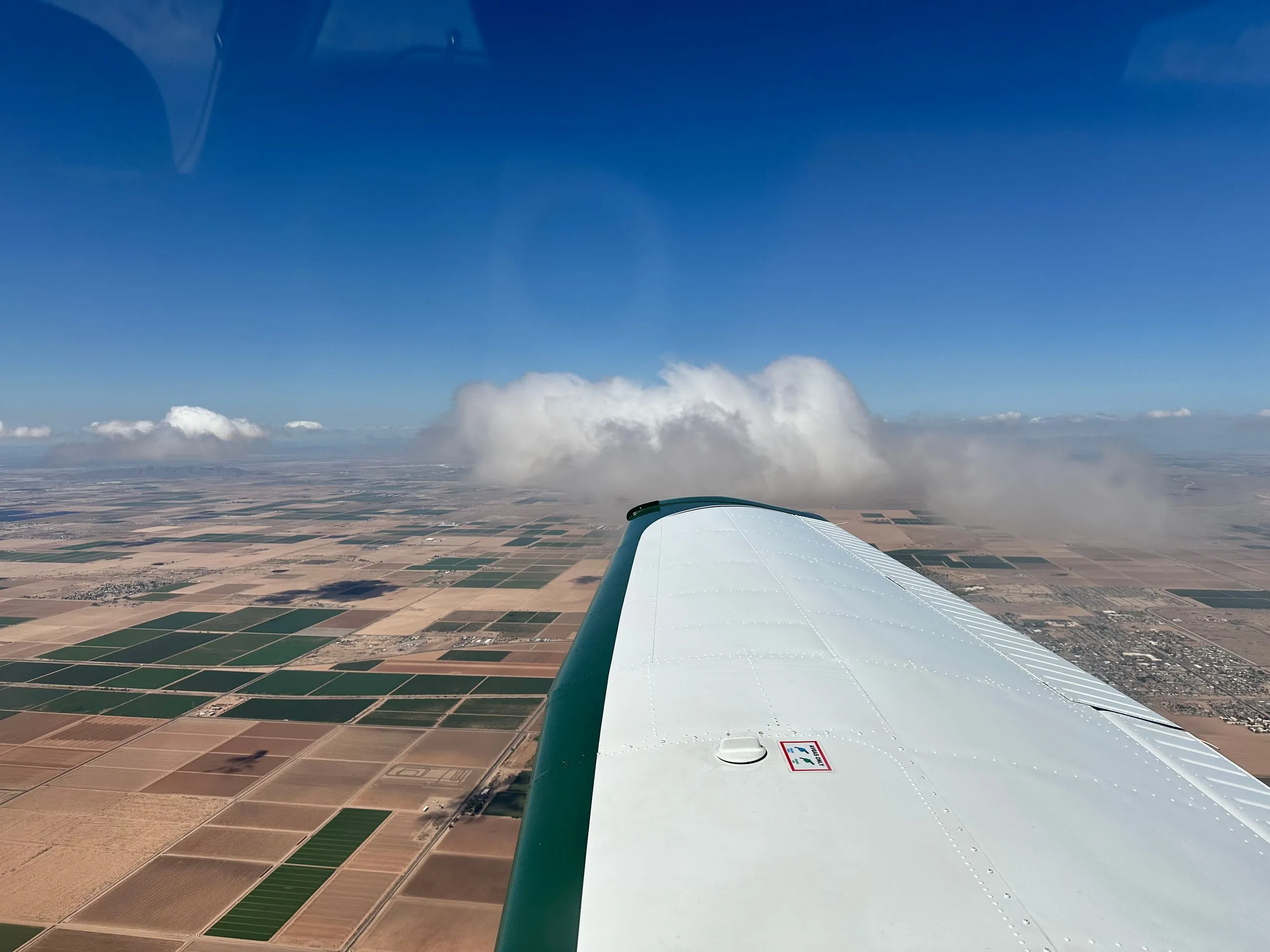 A lone cloud over green farm fields, past the wing